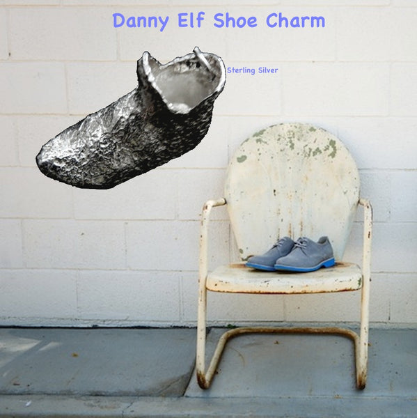 On a background of a rusty white metal lawn chair, white wall and slate floor, purple shoes on white chair next to Elf Shoe.This textured Elf Slipper Shoe is enough to make your toes curl! Straight from "I Dream of Jeannie", (and The North Pole!) this whimsical large charm has beautiful lines and nearly resembles the magic lamp, itself! Even if the shoe doesn't fit...you can still wear it! Equally fun as a single charm on a bracelet as it is around your neck! Sterling silver textured elf shoe 3D charm with 