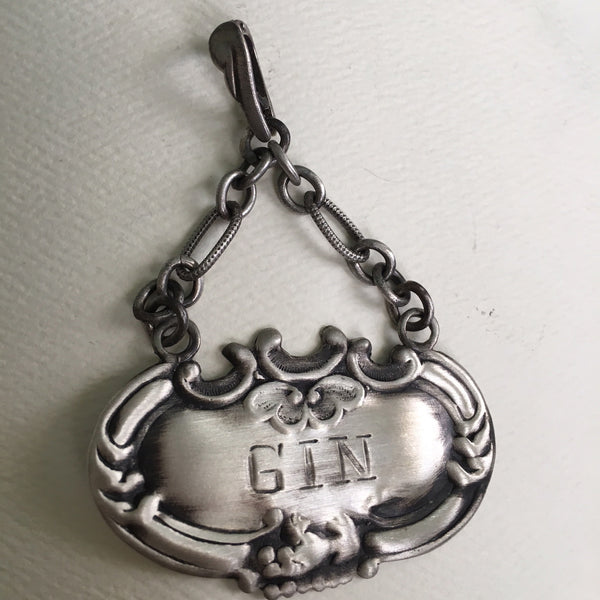 Meant to adorn a neck of a different kind, this Gin Tag adapts beautifully, and why NOT? With its beautiful 2" of on of my most favorite chains attached to the perfect bail, which opens and snaps over beads or pearls easily or slips through the most rugged chain. Engraved and ornate and available in either shiny or my vintage oxidized finish. Even teetotalers like this!  (Chains sold separately.)  1-3/4" x 1" x 2" approximately.  Sterling Silver Gin Tag  Charm. Comes with black leather cord. Made in the USA